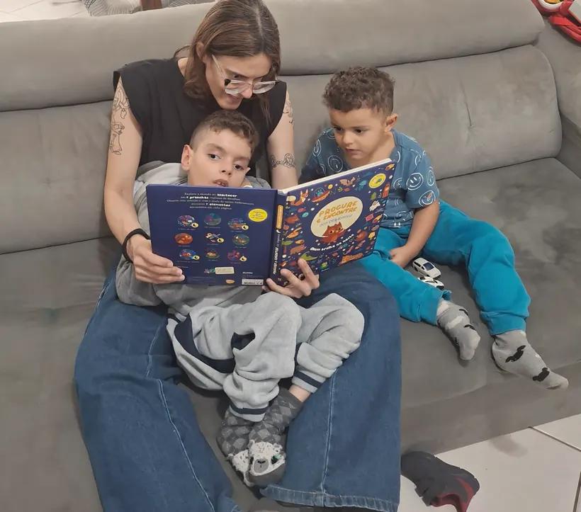 Rafaela Cruz lendo um livro com os dois filhos no sofá de casa